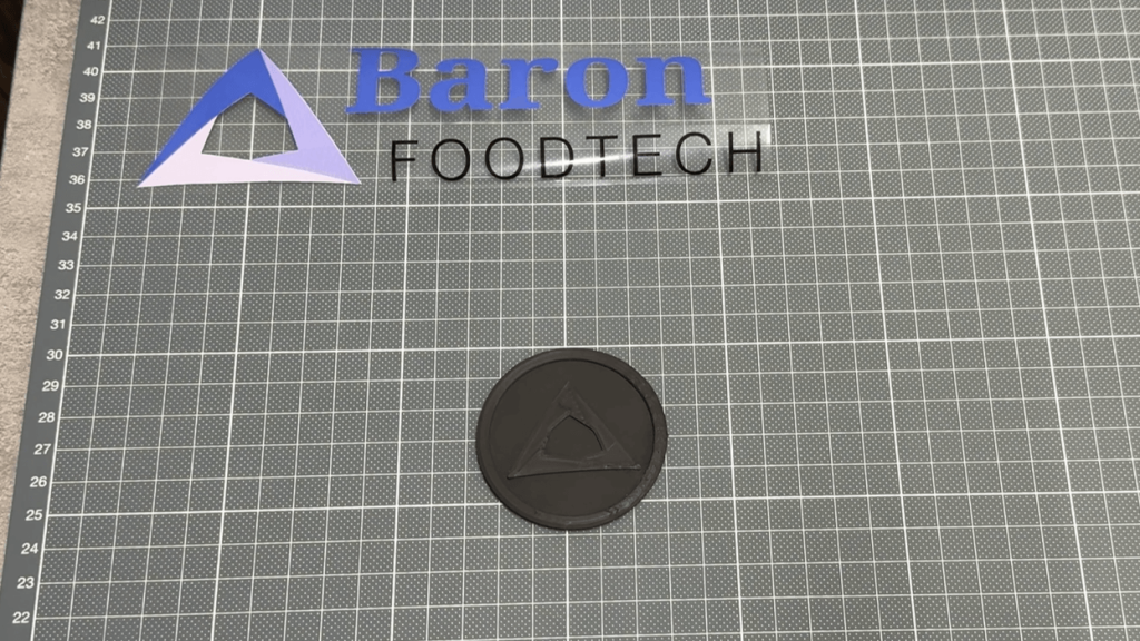 A 3D printed prototype part with the Baron Foodtech logo in the background.